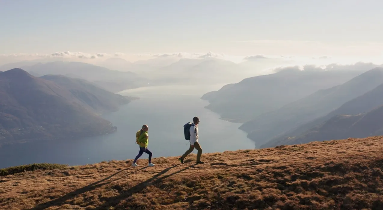 Two people walking on a mountain ridge overlooking a Swiss lake at dawn